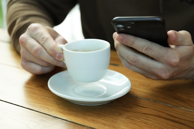 L'homme boit du café et tient le téléphone, gros plan