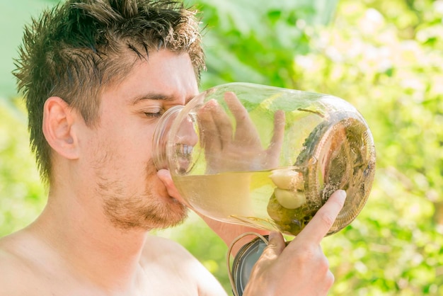 L'homme boit la saumure du pot avec des concombres marinés