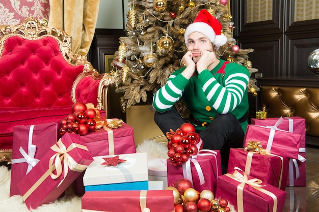 Homme avec des boîtes présentes à l'arbre de Noël. L'homme prépare des packs de cadeaux le soir du nouvel an. L'homme en costume de père Noël fête le nouvel an. Le Père Noël s'arrête ici.