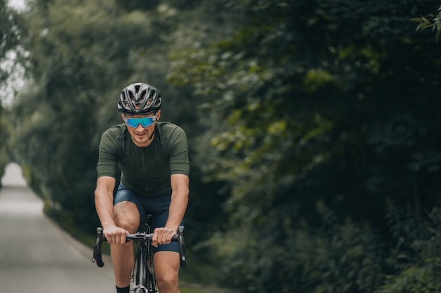 Homme en bonne santé et en forme faisant du vélo sur la route au milieu de la nature verdoyante