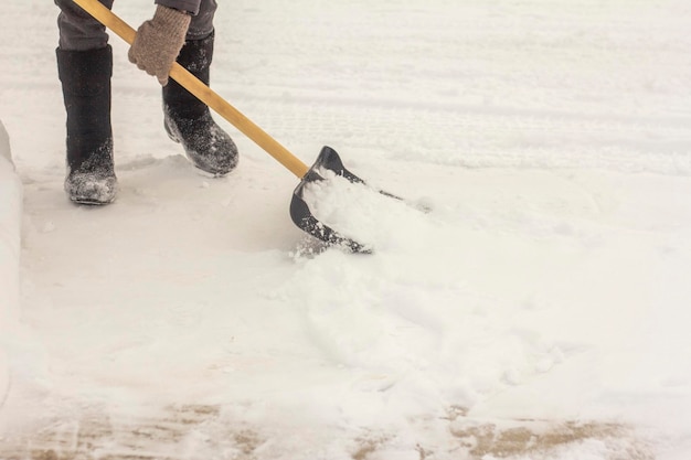Un homme en bottes de feutre, une pelle à la main, enlève la neige du trottoir après une chute de neige.