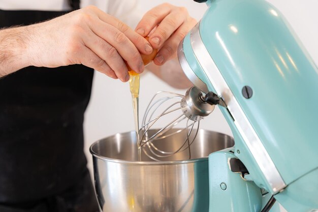 Un homme boulanger cuisinant un gâteau de velours rouge à la maison préparant le gâteau en ajoutant des œufs dans la machine à travailler à la maison