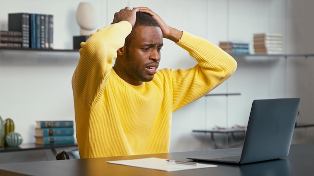 Un homme bouleversé regarde un ordinateur portable avec une connexion Internet perdue, tenant les mains sur la tête, assis au bureau
