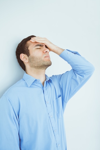 Photo homme bouleversé les yeux fermés et une main sur le front appuyé contre un mur