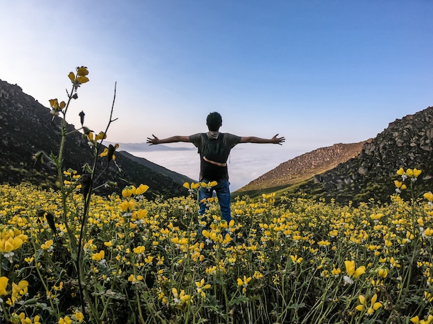 homme à bras ouverts debout sur un paysage de fleurs d'une vallée montagneuse