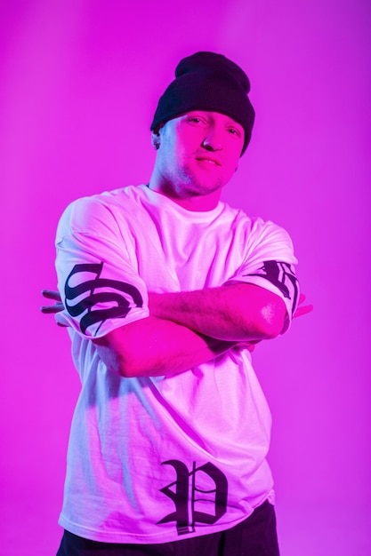 Homme de breakdance de mode à la mode cool avec chapeau et chemise blanche pose dans un studio coloré créatif avec lumière rose et néon