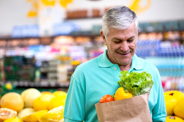 Homme brésilien heureux positif sain tenant un sac à provisions en papier plein de légumes.