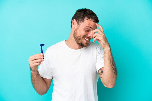 Homme brésilien rasant sa barbe isolé sur fond bleu en riant