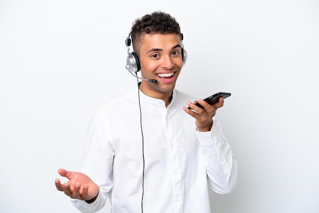 Homme brésilien télévendeur travaillant avec un casque isolé sur fond blanc en gardant une conversation avec le téléphone mobile avec quelqu'un