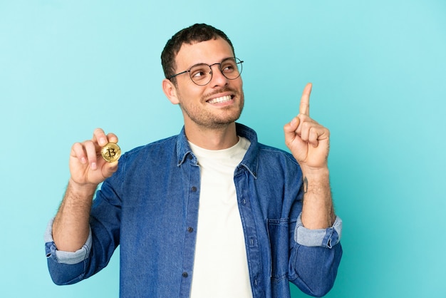 Homme brésilien tenant un Bitcoin sur fond bleu isolé pointant vers une excellente idée