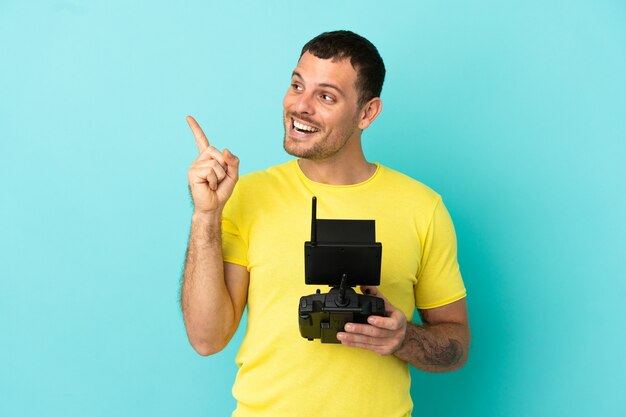 Homme brésilien tenant une télécommande de drone sur fond bleu isolé dans l'intention de réaliser la solution tout en levant un doigt vers le haut