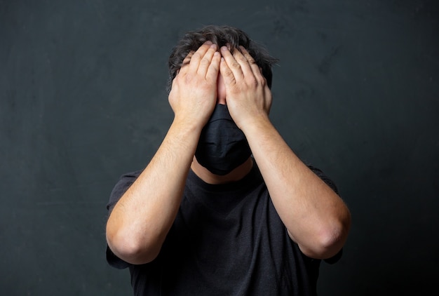 Homme brun fatigué en masque noir sur mur sombre