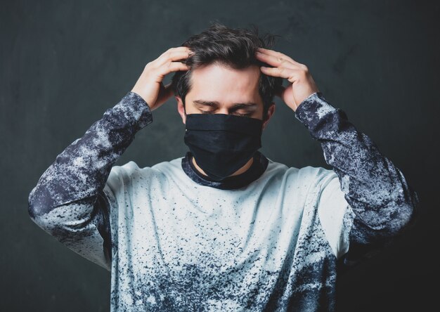 Homme brun fatigué en masque noir sur mur sombre