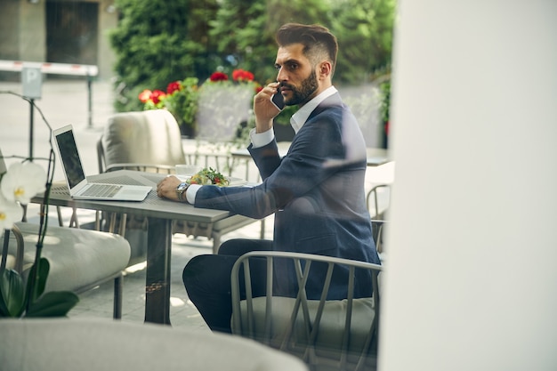 Homme brune attentif assis en position semi à la table et déjeunant pendant le travail à distance