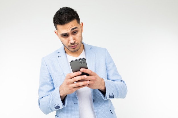 Homme brune élégante dans une veste classique bleue regarde attentivement un smartphone sur un blanc