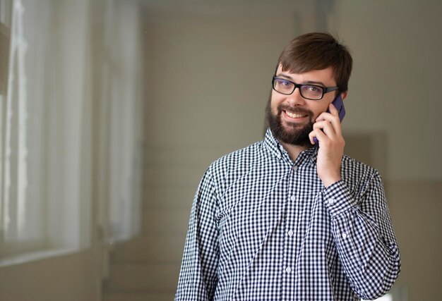 Homme brune souriante dans des verres pour la vision debout et parlant au téléphone en regardant la caméra