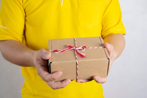 Homme brune tenant une boîte de papier dans les deux mains portant un polo jaune avec un fond blanc