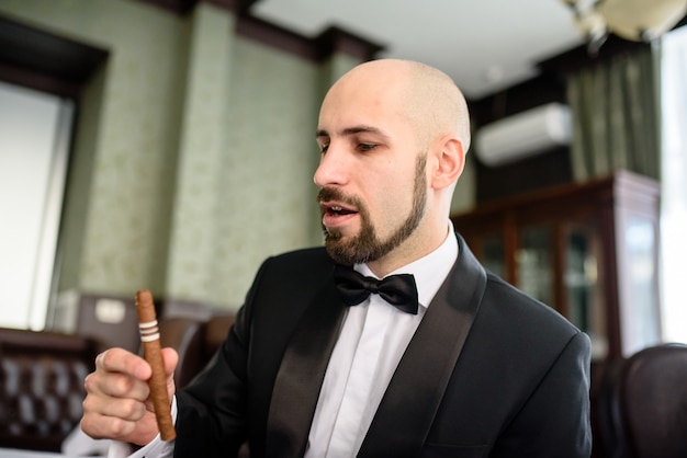 Un homme brutal dans un manteau de robe fume un cigare.