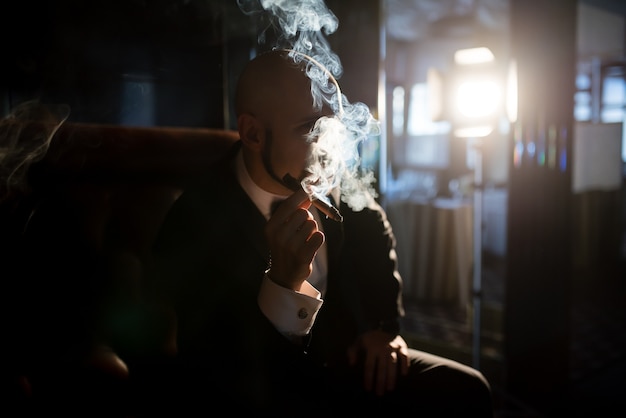 Un homme brutal dans un manteau de robe fume un cigare.