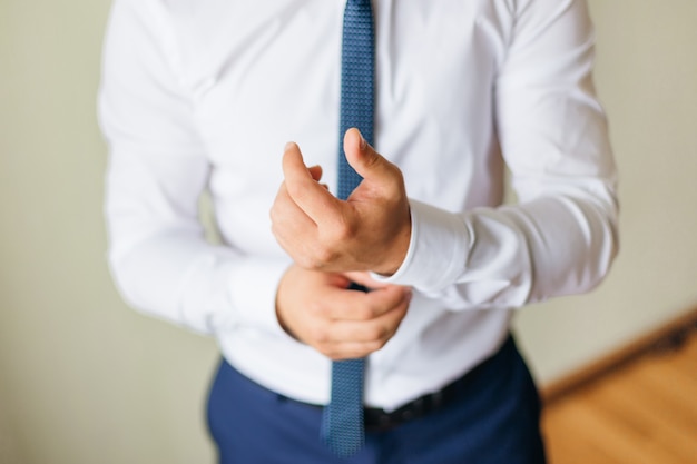 Un homme de bureau en chemise blanche et cravate bleue fixe les poignets. marié élégant.