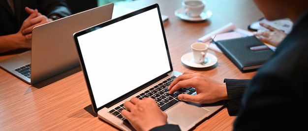 Un homme de bureau utilise un ordinateur portable avec un écran blanc sur le bureau en bois.