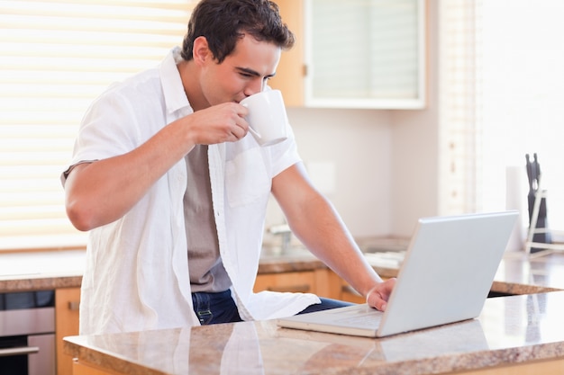 Homme buvant du café tout en travaillant sur son ordinateur portable dans la cuisine