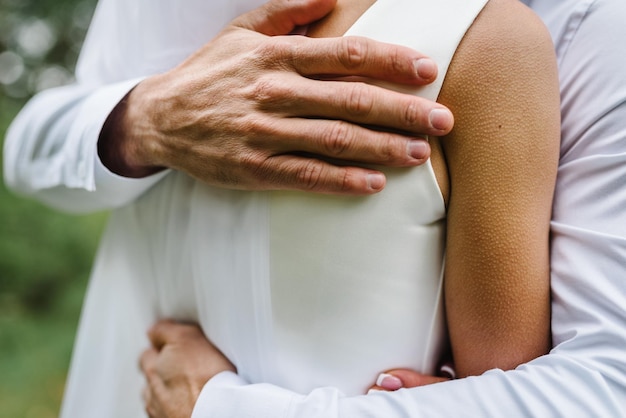 Homme câlin femme La chair de poule est apparue sur le corps d'une belle jeune mariée de toucher l'homme Belle texture de la peau Un marié embrasse doucement la fille dans une robe de mariée par les épaules à la chair de poule Gros plan