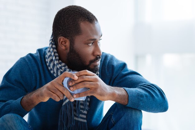 Homme calme. Homme réfléchi strict et fiable regardant vers le côté gauche tout en étant assis tranquillement avec une tasse de thé