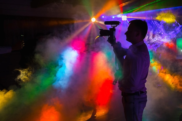 Un homme avec une caméra tourne une vidéo dans une discothèque avec des rayons de néon