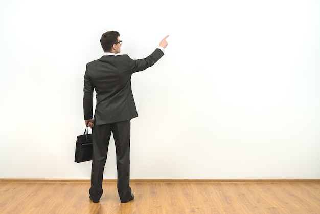 L'homme avec un cas faisant des gestes sur le fond de mur blanc