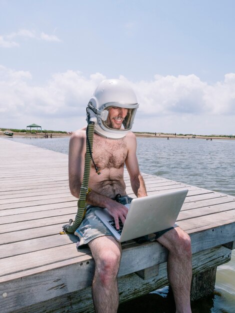 Homme avec casque d'astronaute et ordinateur portable sur la plage