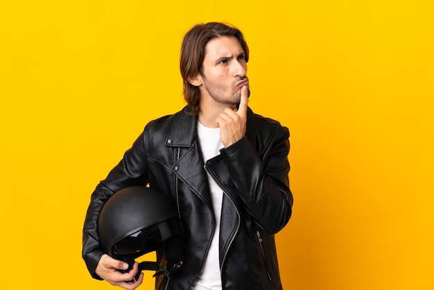 Homme avec un casque de moto isolé sur fond jaune ayant des doutes tout en levant les yeux