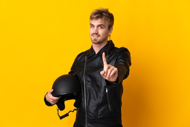 Homme avec un casque de moto isolé sur fond jaune montrant et soulevant un doigt