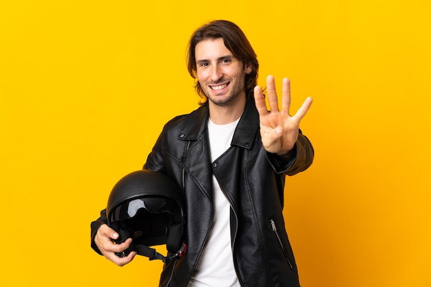 Homme avec un casque de moto isolé sur mur jaune heureux et comptant quatre avec les doigts