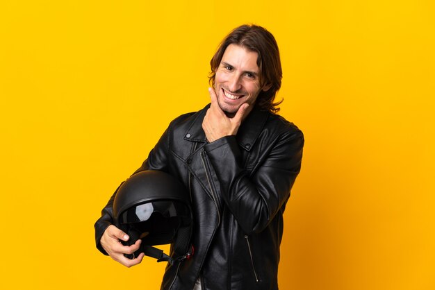 Homme avec un casque de moto isolé sur mur jaune heureux et souriant