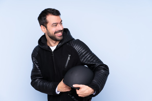 Homme avec un casque de moto sur un mur isolé avec les bras croisés et heureux