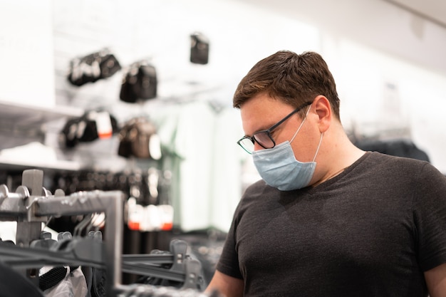 Homme caucasien, acheter des vêtements avec masque médical. Nouveau concept normal.