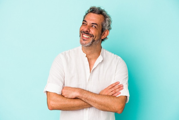 Homme caucasien d'âge moyen isolé sur fond bleu souriant confiant avec les bras croisés.