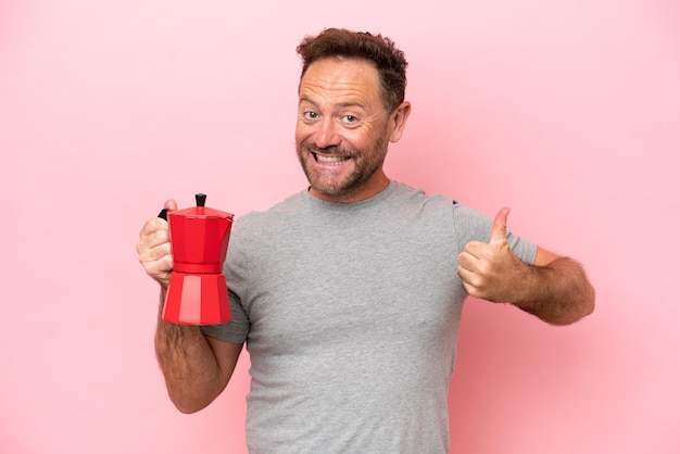 Homme caucasien d'âge moyen tenant une cafetière isolée sur fond rose avec les pouces vers le haut parce que quelque chose de bien s'est produit