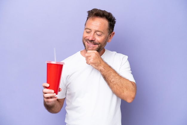 Homme caucasien d'âge moyen tenant un soda isolé sur fond violet regardant sur le côté et souriant