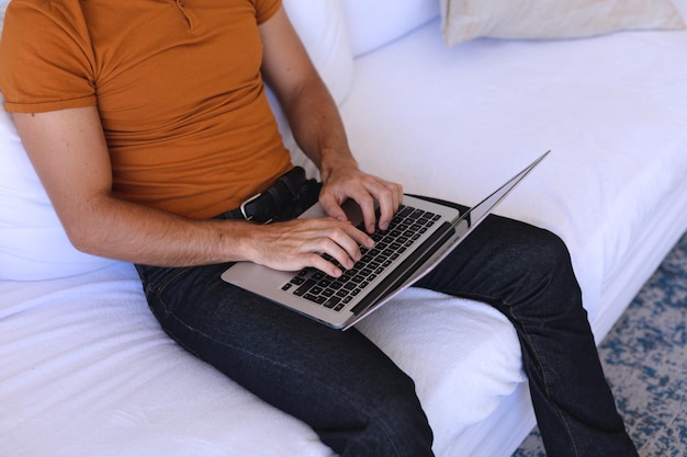 Homme caucasien assis sur un canapé à l'aide d'un ordinateur portable