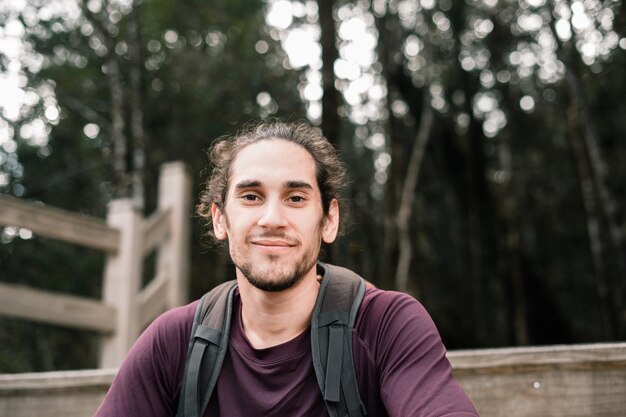 Un homme caucasien à la barbe assis sur une jetée en bois regardant la caméra souriant heureux et content