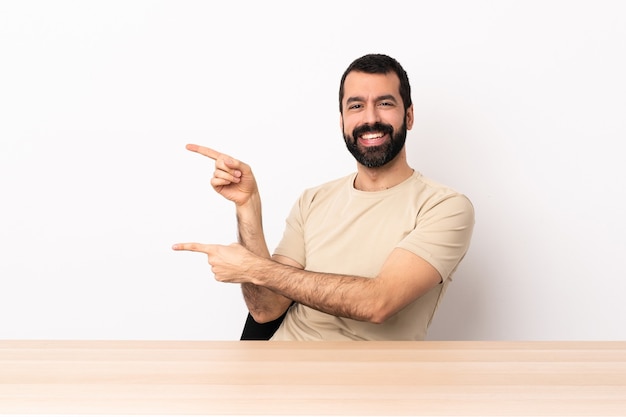 Homme caucasien avec barbe dans une table pointant le doigt sur le côté et présentant un produit.