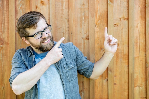 Un homme caucasien barbu souriant montre un geste avec son index pointant vers le haut