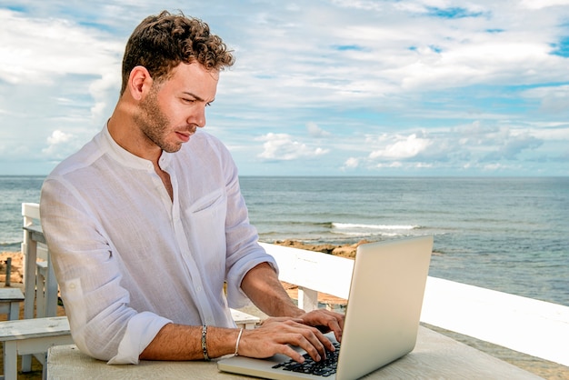 Homme caucasien beau et réussi dans un élégant bien habillé travaillant avec un ordinateur portable sur la plage. Étudiant indépendant et travail à distance.businessman sur la rive méditerranéenne