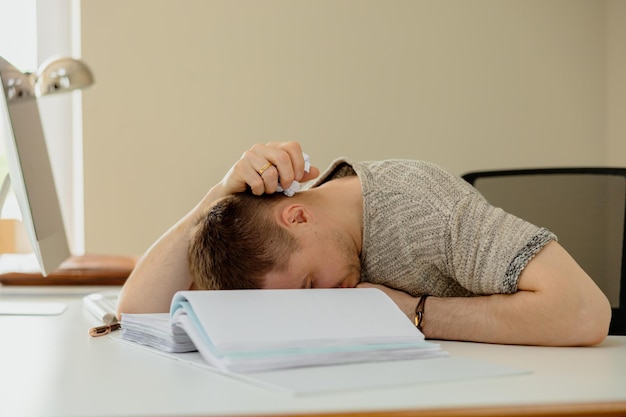 Homme caucasien déprimé avec des maux de tête assis à son bureau dans le bureau Un jeune employé stressé a des problèmes au travail L'homme d'affaires a l'épuisement professionnel La santé mentale