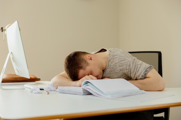 Homme caucasien déprimé avec des maux de tête assis à son bureau dans le bureau Un jeune employé stressé a des problèmes au travail L'homme d'affaires a l'épuisement professionnel La santé mentale
