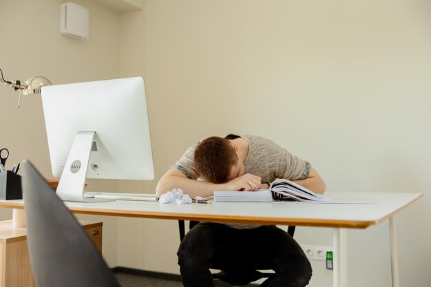 Homme caucasien déprimé avec des maux de tête assis à son bureau dans le bureau Un jeune employé stressé a des problèmes au travail L'homme d'affaires a l'épuisement professionnel La santé mentale