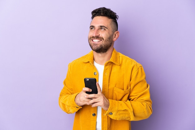 Homme caucasien isolé sur fond violet à l'aide de téléphone mobile et levant