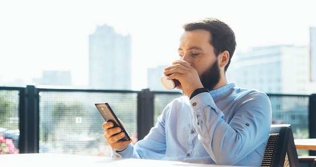 Homme caucasien occupé avec barbe à discuter au téléphone tout en buvant une tasse de café à la cafétéria